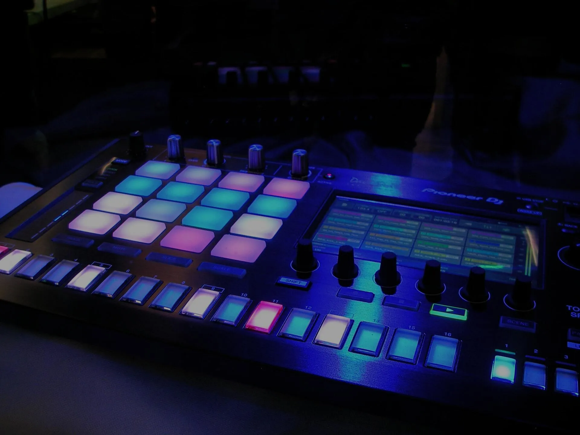 A music production controller glowing with colourful pads in a darkened studio
