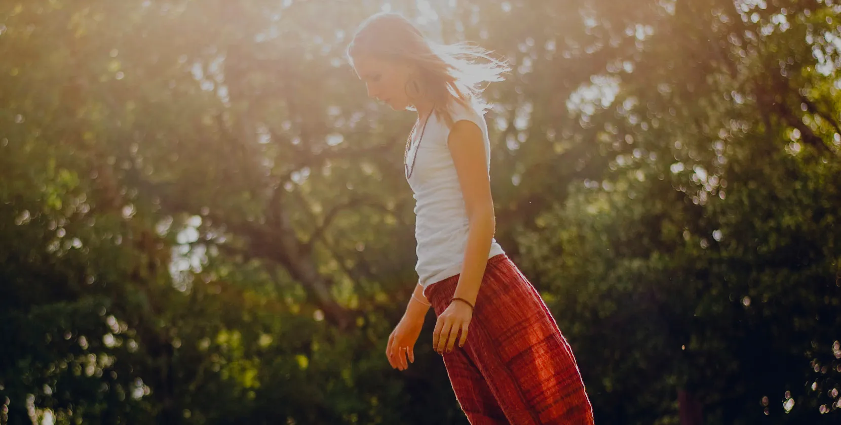 A young person walking through sunlit trees at golden hour, calm and unhurried